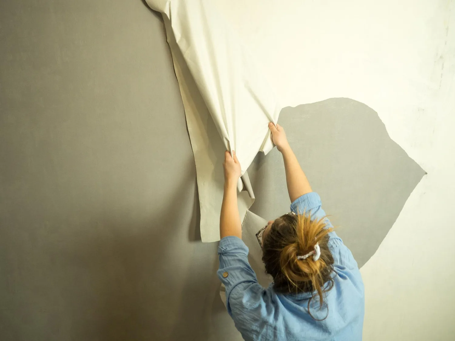 Une femme déchire le vieux papier peint et fait des rénovations dans l'appartement